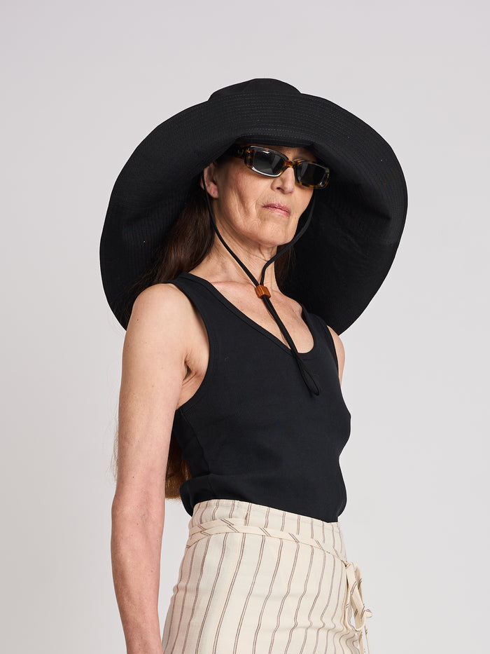 The Lucie Marquis 'Dylan Sunhat' is a wide brimmed sun hat made from high quality cotton twill with heavy topstitching and a wooden block cord end. Inspired by the iconic spirit of Bob Dylan and the bold essence of Georgia O'Keeffe, the sun hat embodies timeless style with a subtle nod to the 70s and a touch of cowboy charm. Perfect for shielding from the sun, it's the ideal accessory for your travel adventures.